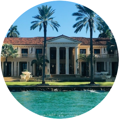 Luxury mansion with palm trees in front of the ocean.