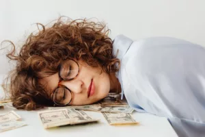 woman with glasses asleep at a desk with money under her head Residual Income Online Business